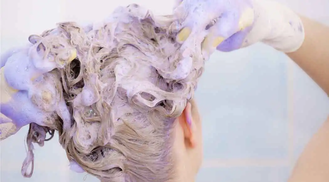 A woman applying purple shampoo to hair