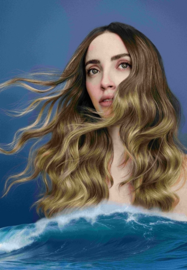 A photo of a woman with shiny golden blonde hair above an ocean wave.